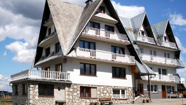 Un immeuble à plusieurs étages doté d’un toit triangulaire au design original, de fondations en pierre et de balcons.