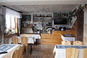 A dining area with wooden chairs and tables, a kitchen counter, and a wall-mounted television. - Pokoje Gościnne Janina  (Zakopane)