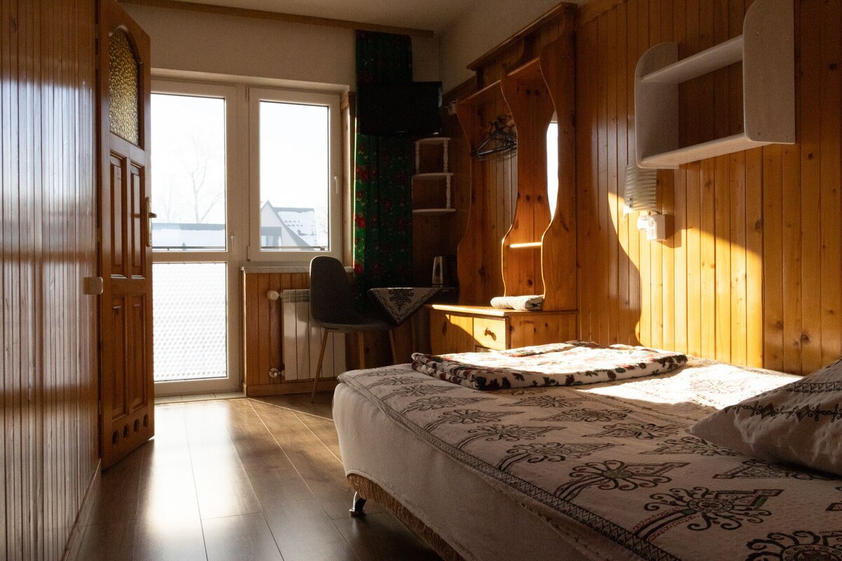 Una habitación de madera con una cama, una silla, un radiador y una ventana.