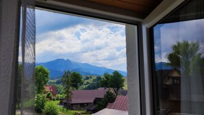 Une vue à travers une fenêtre, avec un paysage de montagne, des bâtiments en bois et un ciel dégagé.
