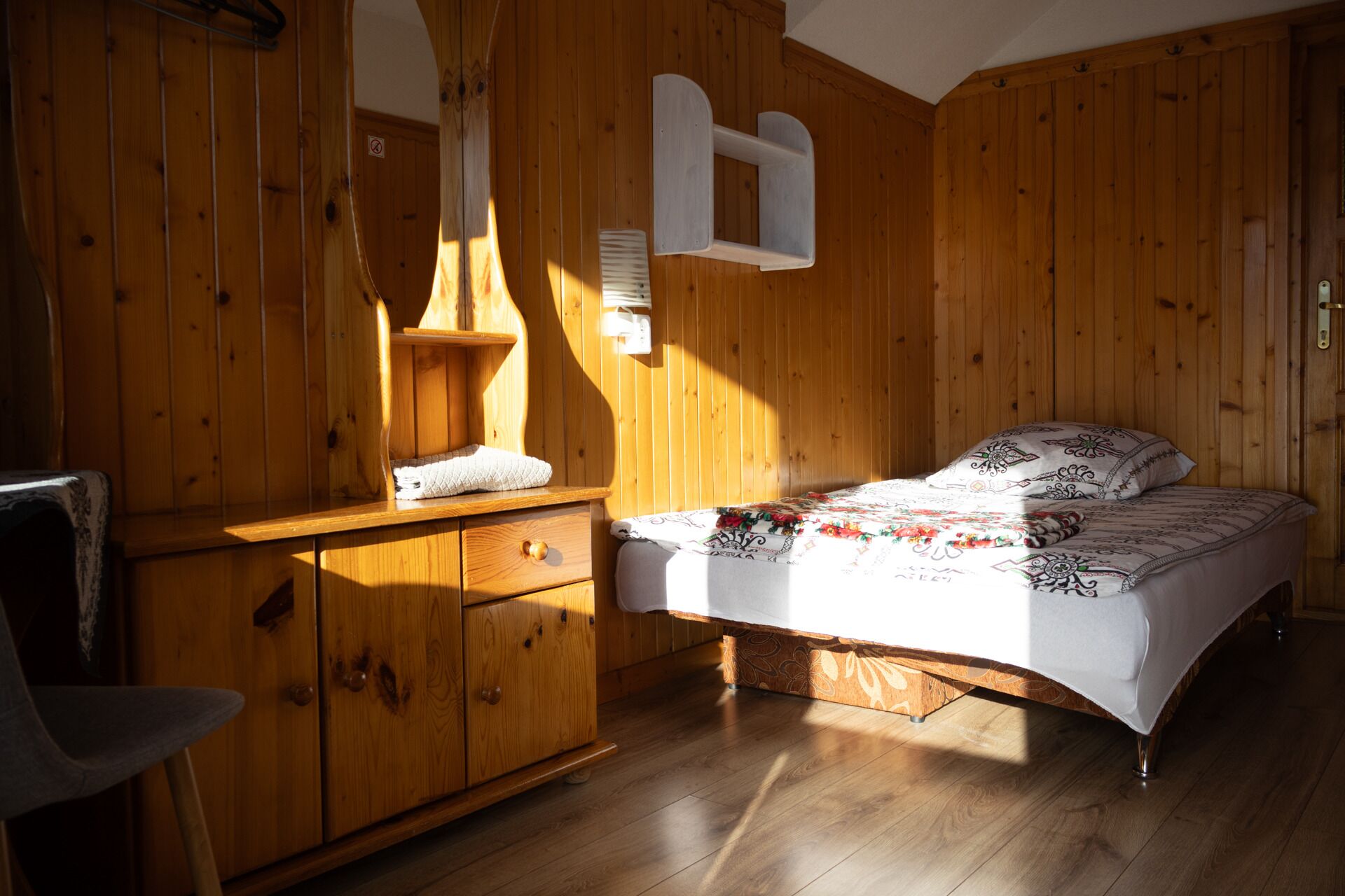 A wooden room with a bed, a dresser, and a mirror.