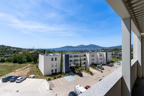Ein mehrstöckiges Gebäude mit Parkplatz, Meerblick und Bergen in der Ferne.