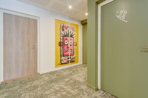 A hallway with a wooden door, a green door, and a wall with a colorful artwork. - Studio La Factory - Avec ventilateur (Reims)