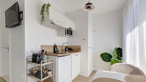 Ett kompakt kök med mikrovågsugn, diskho och ett litet kylskåp. En tv är monterad på väggen, och en växt syns.