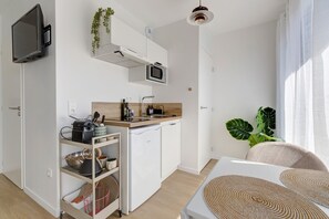 A compact kitchen with a microwave, sink, and a small refrigerator. There is a TV mounted on the wall, and a plant is visible. - Studio La Factory - Avec ventilateur (Reims)