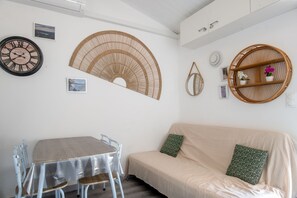 A room with a round dining table, a sofa, and wall-mounted wicker decor. - Mazet de Soleil - Maisonnette climatisée pour 4 (Saint-Martin-de-Brômes)