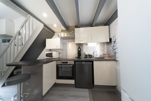 A modern kitchen with a microwave, oven, dishwasher, and a bar stool. - Mazet de Soleil - Maisonnette climatisée pour 4 (Saint-Martin-de-Brômes)