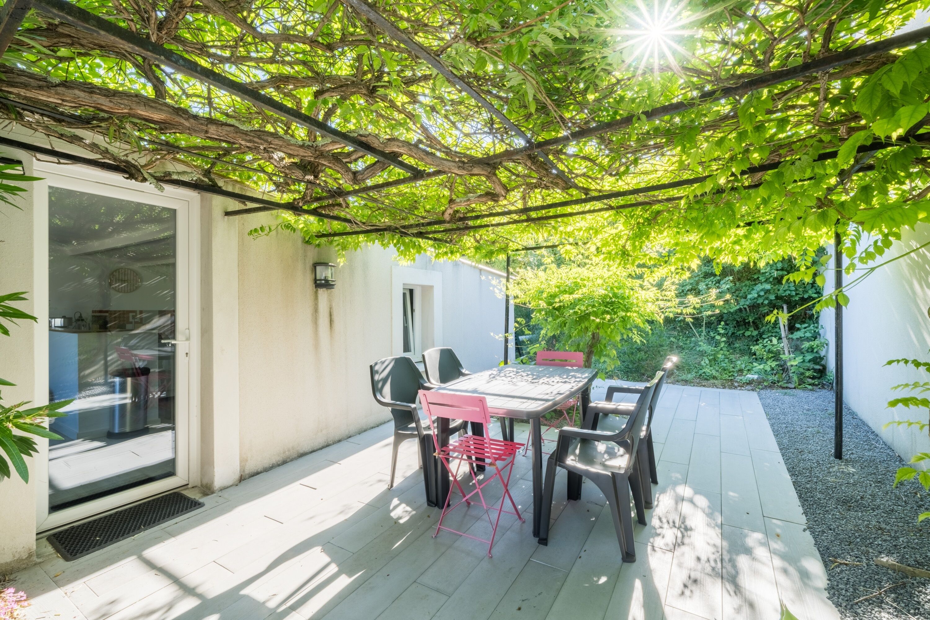 Une terrasse avec une table et des chaises, une porte vitrée et un espace jardin.