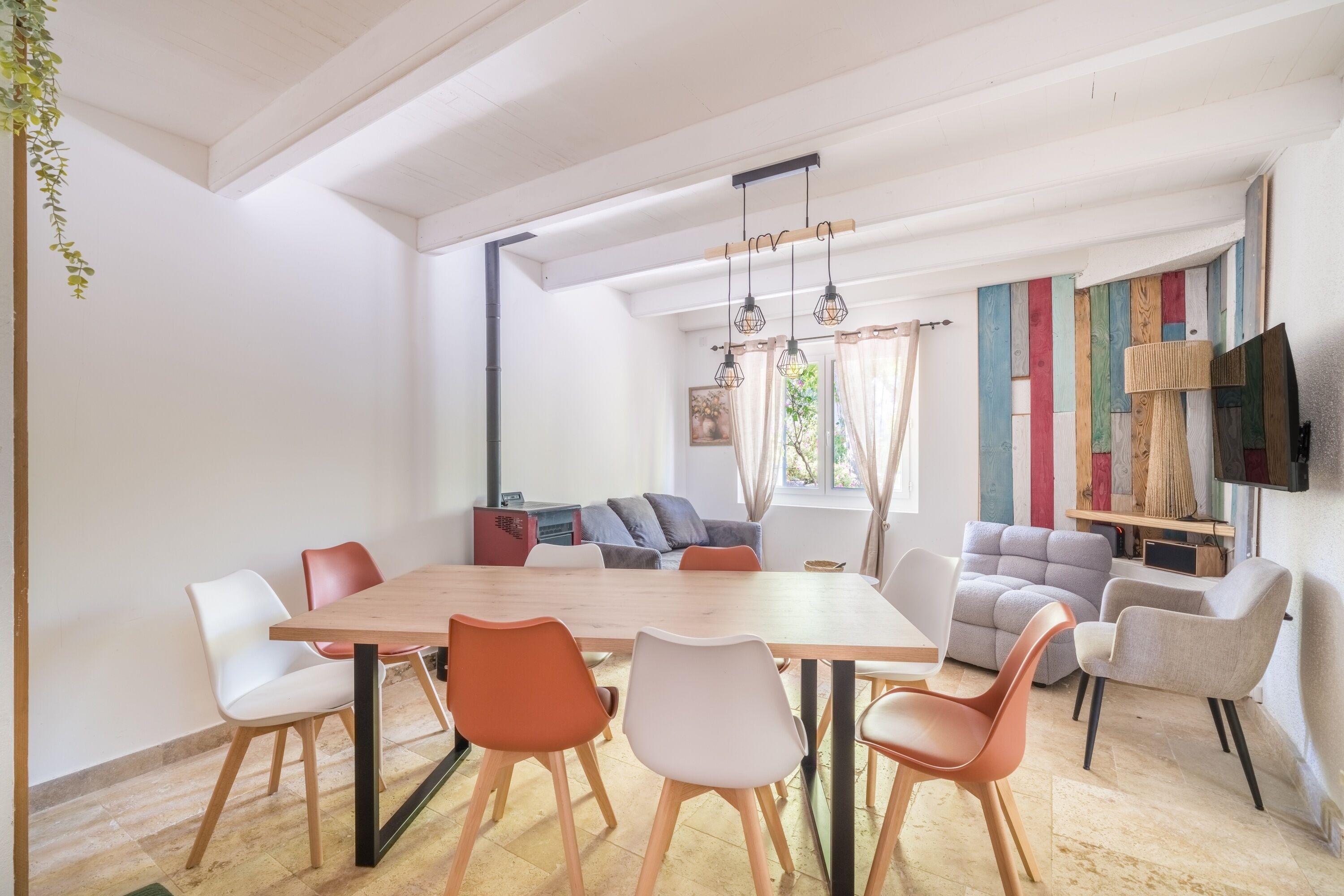 Un comedor moderno con una mesa y sillas de madera, un sofá y un televisor montado en la pared.