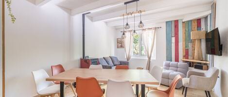 Un comedor moderno con una mesa y sillas de madera, un sofá y un televisor montado en la pared.
