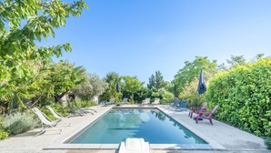 Ein rechteckiger Swimmingpool mit einer weißen, schwimmenden Liege in der Mitte, umgeben von Liegestühlen und Sonnenschirmen.
