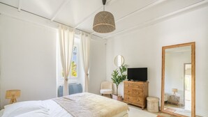Ein Schlafzimmer mit Bett, Kommode, Fernseher, Spiegel und einem Fenster mit Vorhängen.