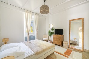 Ett sovrum med en säng, en byrå, en tv, en spegel och ett fönster med gardiner.