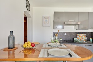 A modern kitchen with stainless steel appliances, a wooden dining table with a fruit bowl, and a framed certificate on the wall. - A l'abri côtier - Appt avec balcon proche plage (Cabourg)