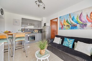 A modern kitchen with a dining area, a sofa, and a colorful sailboat painting on the wall. - A l'abri côtier - Appt avec balcon proche plage (Cabourg)