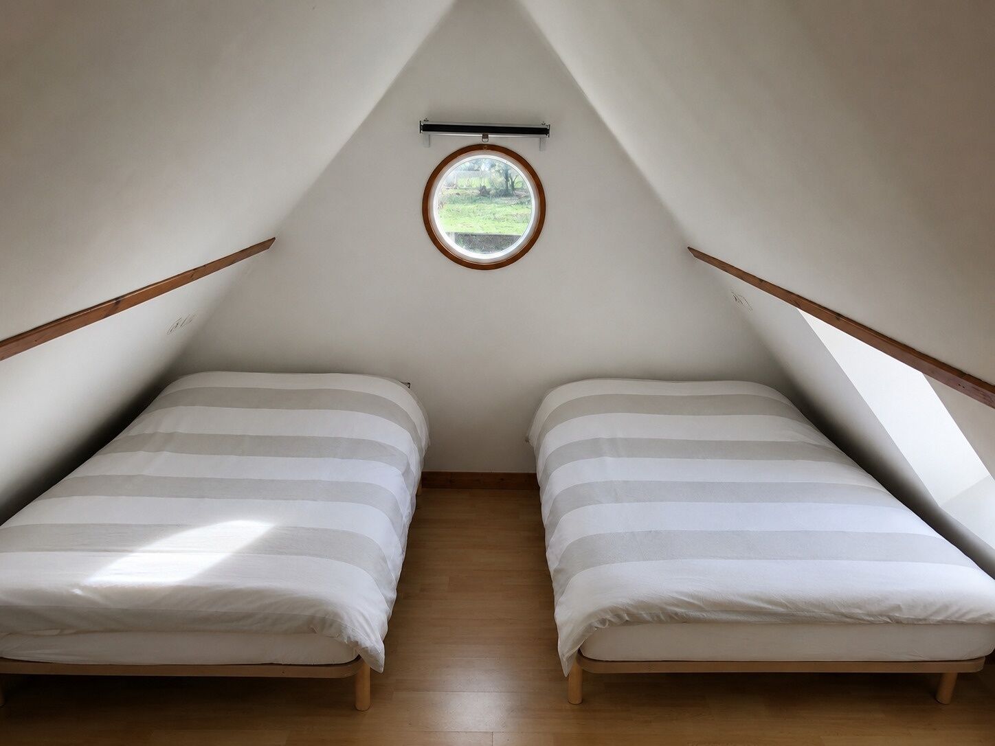 A small attic bedroom with two beds, a skylight, and wooden beams.