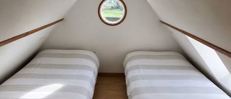 A small attic bedroom with two beds, a skylight, and wooden beams.