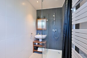 Ein modernes Badezimmer mit Duschkabine aus Glas, einem weißen Waschbecken und einem Holz-Waschtisch.