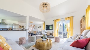 Ein modernes Wohnzimmer mit einer Couch, Hocker, einem Couchtisch und einer Küche im Hintergrund.