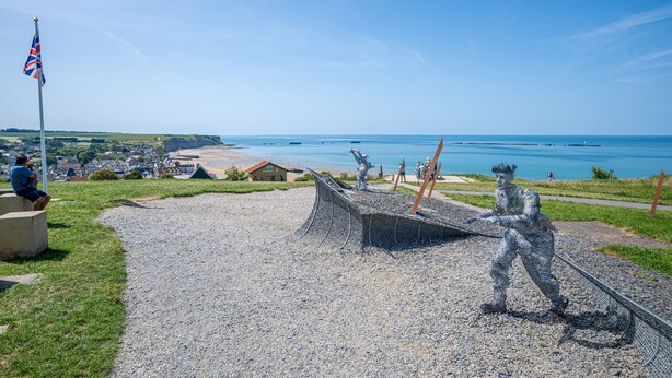 Ein Küstenskulpturengarten mit einer markanten Skulptur, einer Flagge und Blick auf das Meer und die Stadt.