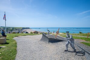 A coastal sculpture garden with a prominent sculpture, a flag, and a view of the sea and town. - Normandie Escape House - À 5 min des plages (Manvieux)