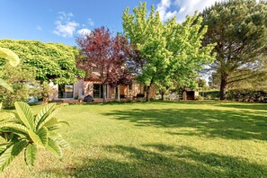 A house with a well-maintained lawn, a large tree, and a building with a porch.