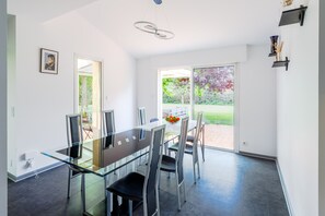 A modern dining area with a glass table, metal chairs, and a view of a garden through a sliding glass door.
