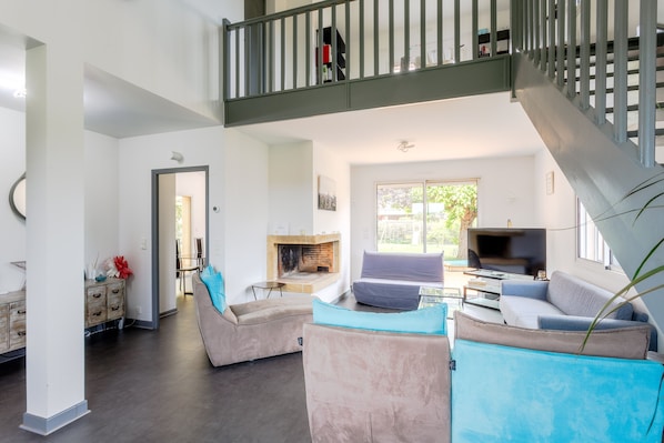 A spacious living area with a fireplace, sofas, a TV, and a staircase.