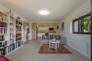Ein modernes Wohnzimmer mit Bücherregal, einer Couch, einem Couchtisch und Blick auf die Küche.