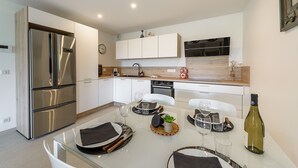 Cozinha moderna com eletrodomésticos de aço inoxidável, armários brancos e uma área de jantar posta para refeição.