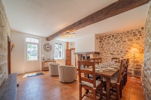 Un espace repas agrémenté d’un mur en pierre, de poutres en bois et d’une grande fenêtre.