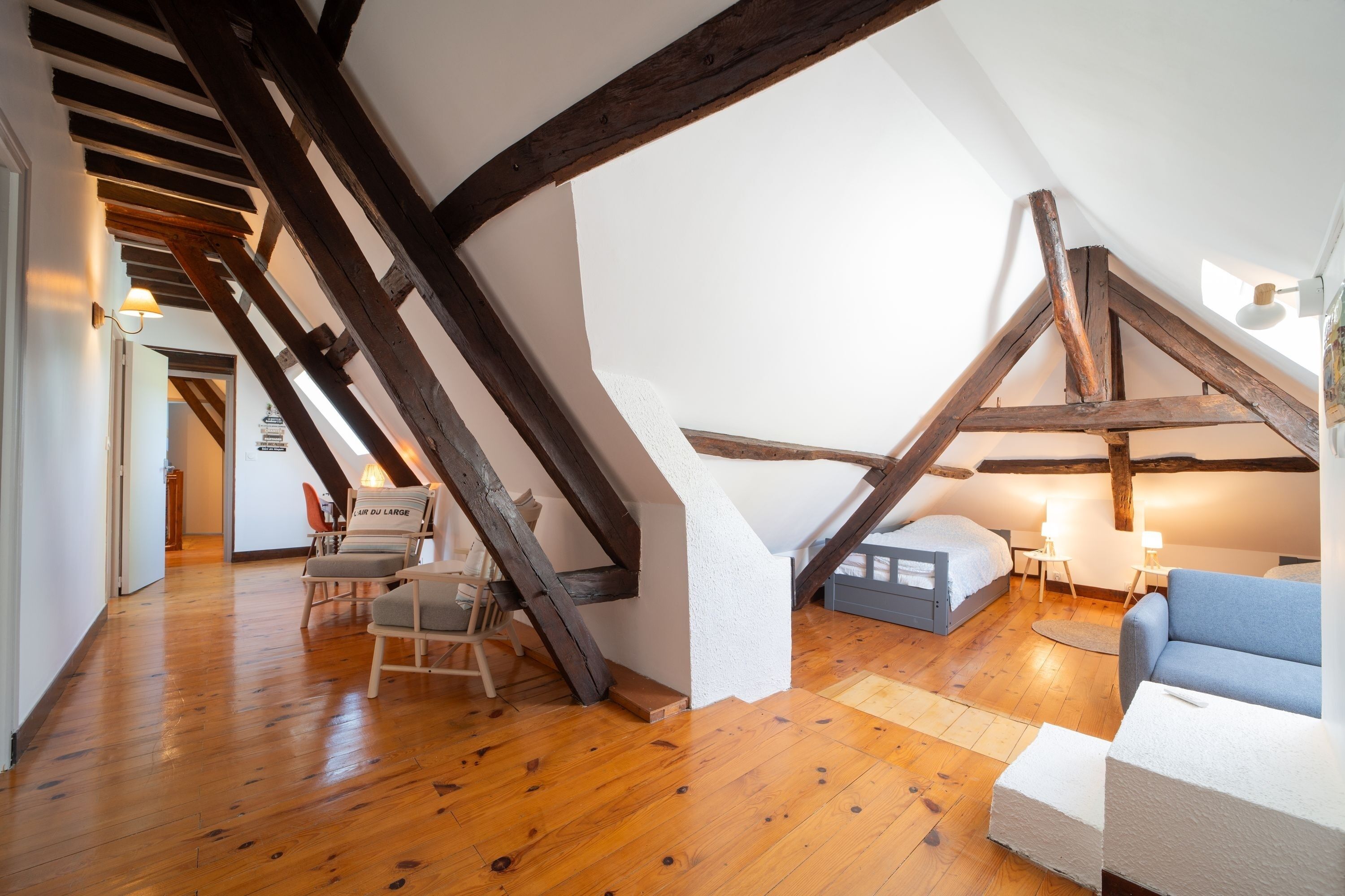 Un dormitori tipus loft amb bigues de fusta al descobert, un llit, un sofà blau i una cadira.