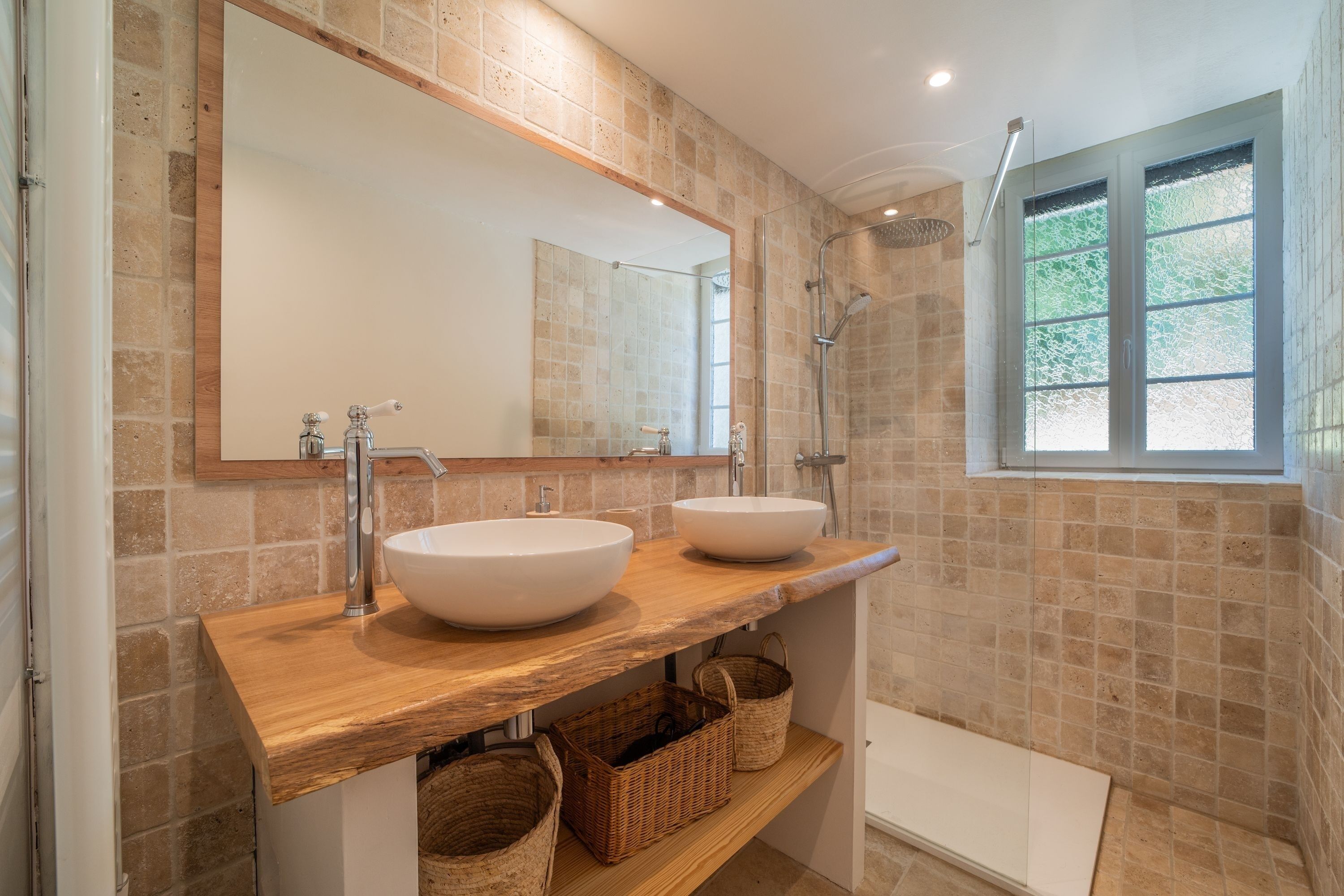 Un baño con dos lavamanos, un espejo grande, una ducha y una ventana.