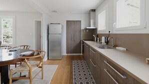 A modern kitchen with a refrigerator, wooden cabinets, a dining table with chairs, and a patterned rug. - Villa ETXEA - À 5 min du port de la Hume (Gujan-Mestras)