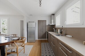 Eine moderne Küche mit Kühlschrank, Holzschränken, einem Esstisch mit Stühlen und einem gemusterten Teppich.