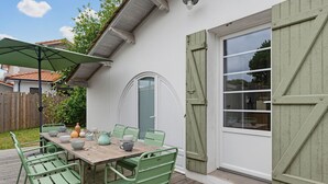 A patio with a wooden table and green chairs, a green umbrella, and a white door with a window. - Villa ETXEA - À 5 min du port de la Hume (Gujan-Mestras)
