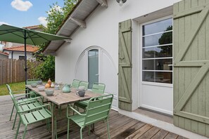 Eine Terrasse mit Holztisch und grünen Stühlen, einem grünen Sonnenschirm und einer weißen Tür mit Fenster.