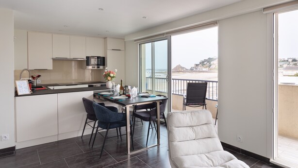 A modern kitchen with a dining area, large windows, and a balcony with a view. - L'as du Val - Avec un accès immédiat sur la plage (Pléneuf-Val-André)