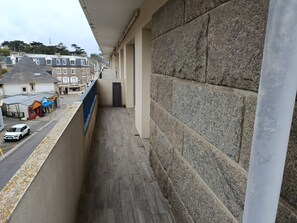 Ein Balkon mit einer Steinmauer, Blick auf eine Straße mit Geschäften und einem parkenden Auto.