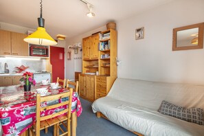 A compact living space with a dining table, wooden cabinets, a sofa, and a hanging lamp. - La Fontaine du Corbeau et Grangettes (Huez)
