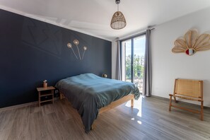 A bedroom with a bed, bedside table, lamp, chair, and a view of the outdoors. - La Villa Sola - Climatisée avec piscine privée (Saint Gilles)
