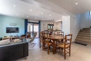 Ein modernes Wohnzimmer mit Fernseher, Sofa und Essbereich mit Holzsesseln und einem Tisch.