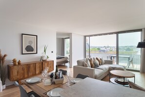 A modern living room with a dining area, a sofa set, and a view through large windows. - Le Madison - À moins d'1 km de la plage (Pléneuf-Val-André)
