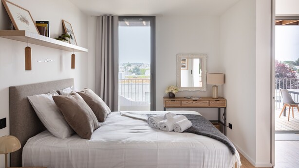Moderni hotellihuone, jossa on suuri sänky, työpöytä lampun kanssa, peili ja näkymä kaupunkiin.