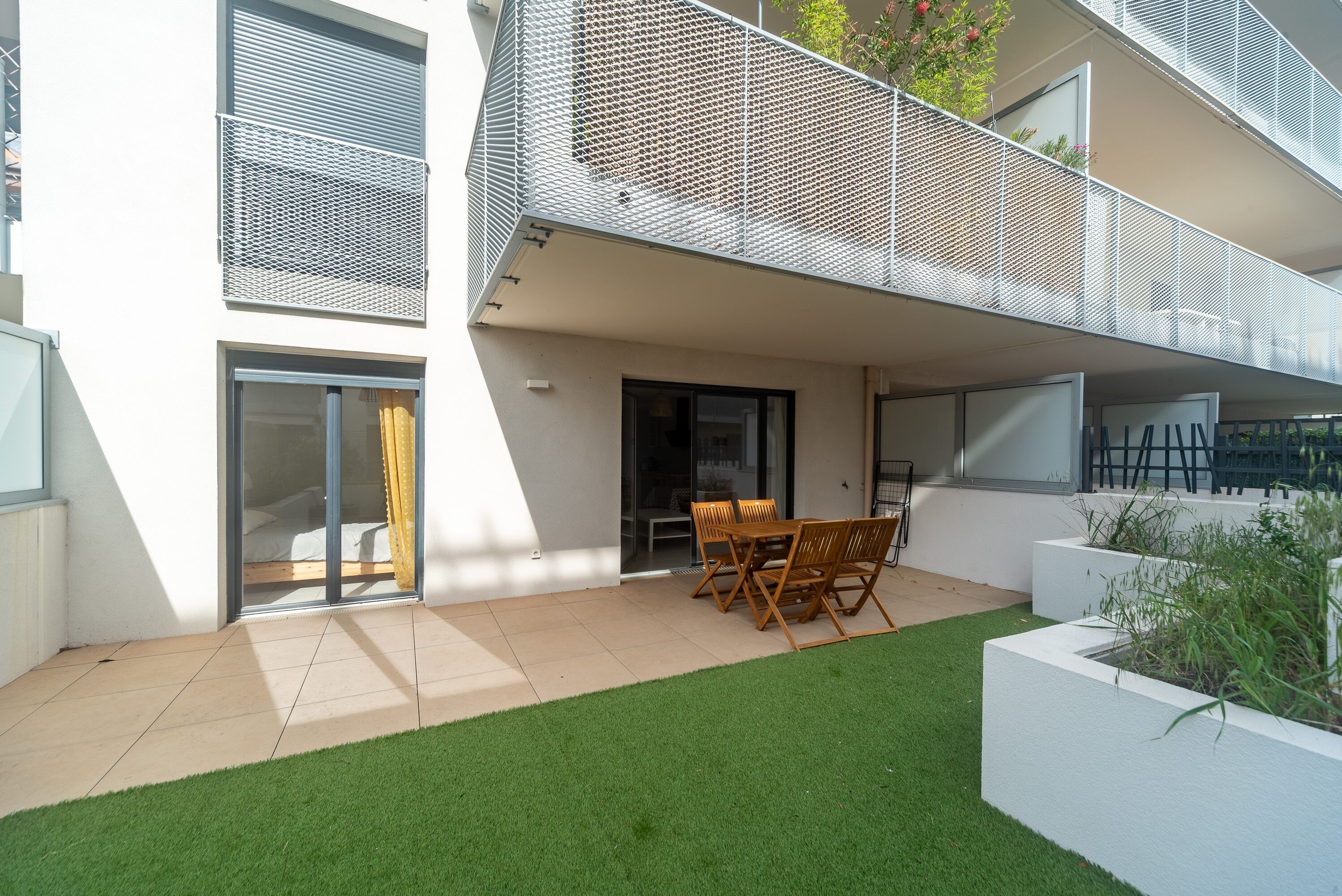 Un edificio moderno con tetto piatto, un balcone con ringhiera a rete e un piccolo patio con tavolo e sedie.