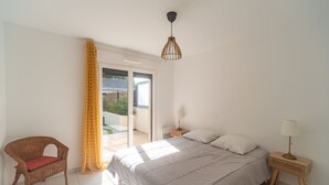 Une chambre à coucher comprenant un lit, une chaise, une table de chevet, une lampe et une porte-fenêtre coulissante donnant sur un espace extérieur.