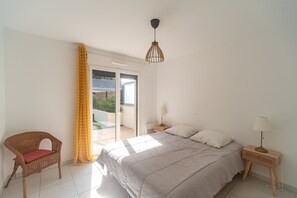 A bedroom with a bed, a chair, a nightstand, a lamp, and a sliding glass door leading to an outdoor area. - Le Lavandou Ensoleillé - Bel appt avec terrasse (Le Lavandou)
