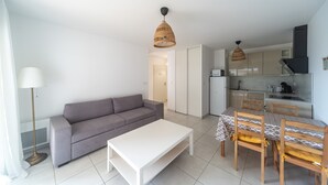 Un salon moderne avec un canapé, une table basse blanche et un coin repas comprenant une table et des chaises. Il y a également un coin cuisine avec des placards et une cuisinière.