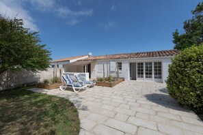 Ein Haus mit einer Terrasse, zwei Liegestühlen, einer Satellitenschüssel und einem Garten.
