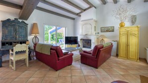 A living room with a fireplace, red leather sofas, a wooden cabinet, and a television. - Le Temps des Vacances - À 500 m de la plage (La Brée-les-Bains)